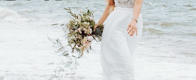 a woman in a white dress holding a bouquet of flowers in the water